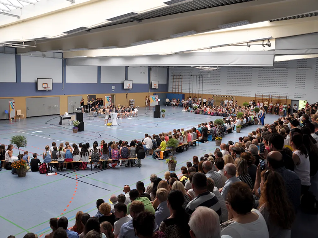 Weiter Blick in die Sporthalle mit Bühne und Publikum.